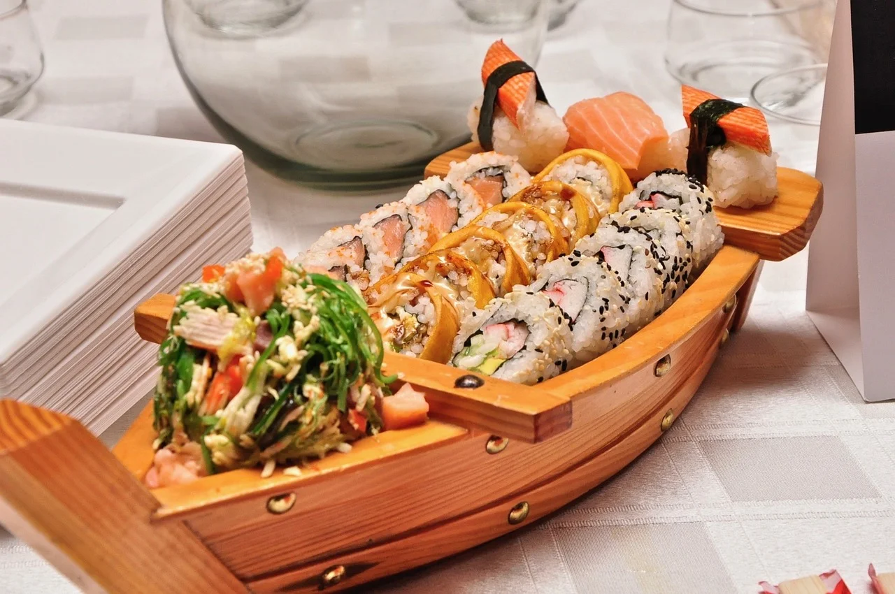 Close-up of a chef's hands using a sharp sushi knife to precisely slice a large, perfectly formed sushi roll, revealing intricate ingredients in sharp detail.